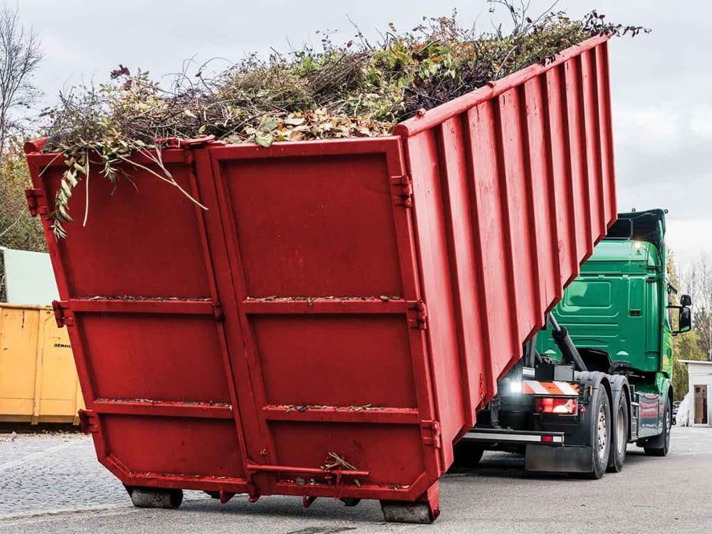 Einen roter Abrollcontainer gefüllt mit Grünschnitt wird von einem LKW des Containerdiensts Eppstein abgeladen.